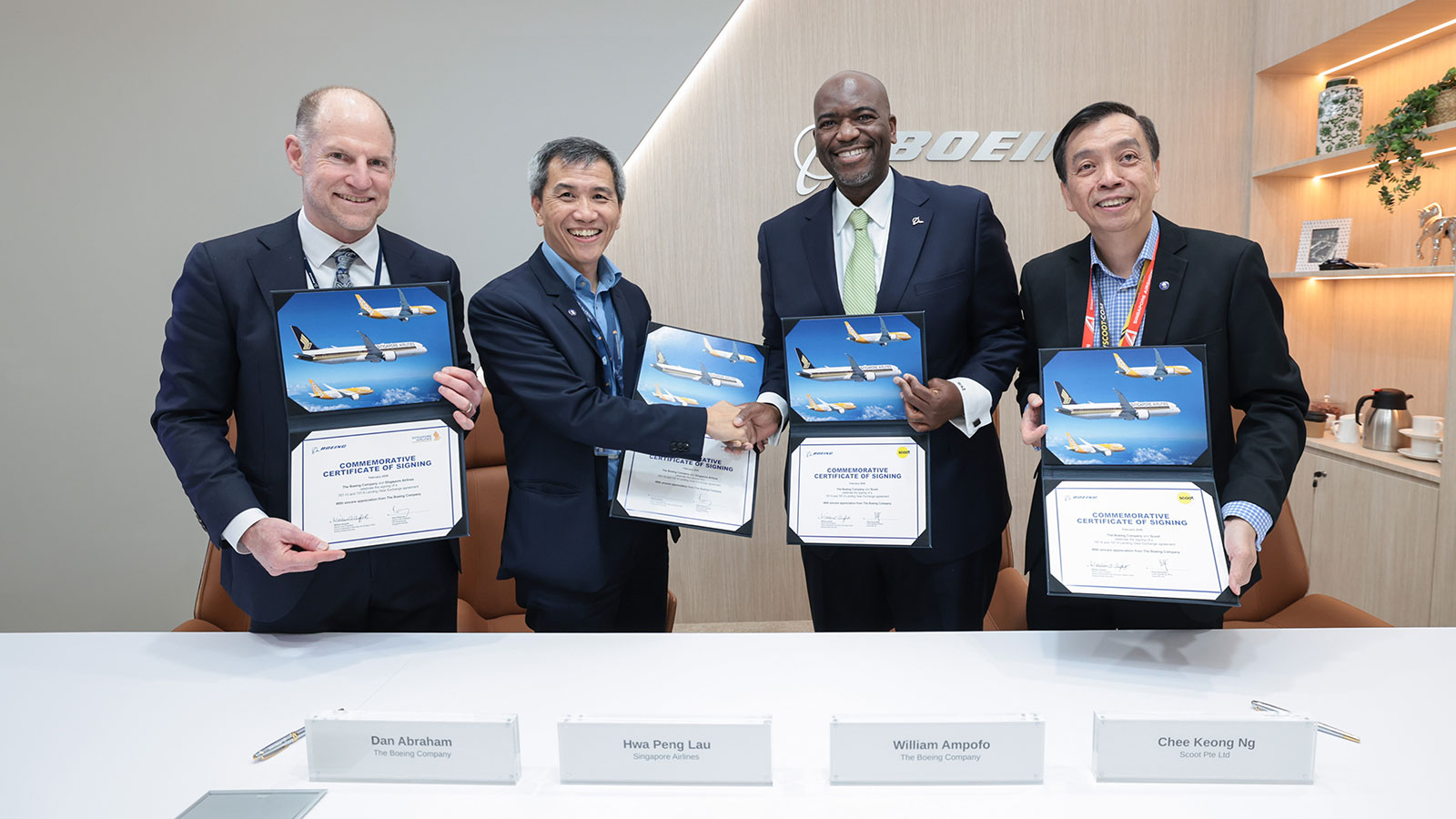 Four men hold up signing certificates and shake hands.