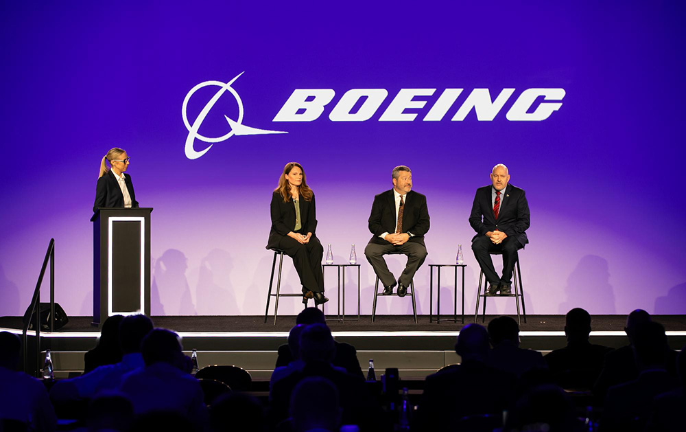 A panel discussion at a Boeing event with four speakers on stage and an audience in the foreground.